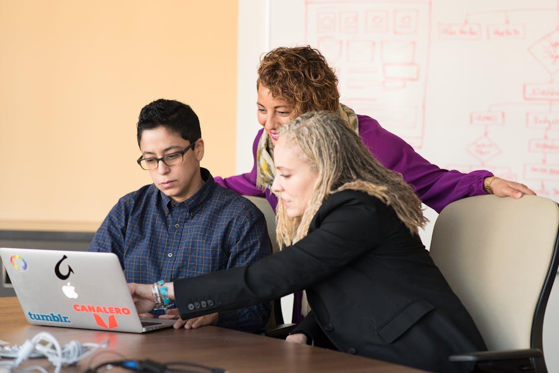 Free Three colleagues collaborating on a laptop in a tech-focused office environment. Stock Photo