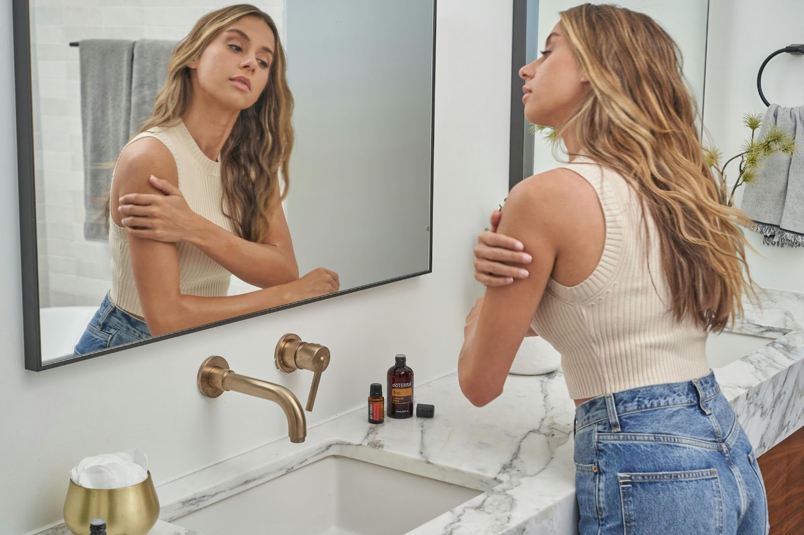 Blonde woman applying body oil to her arms after a shower