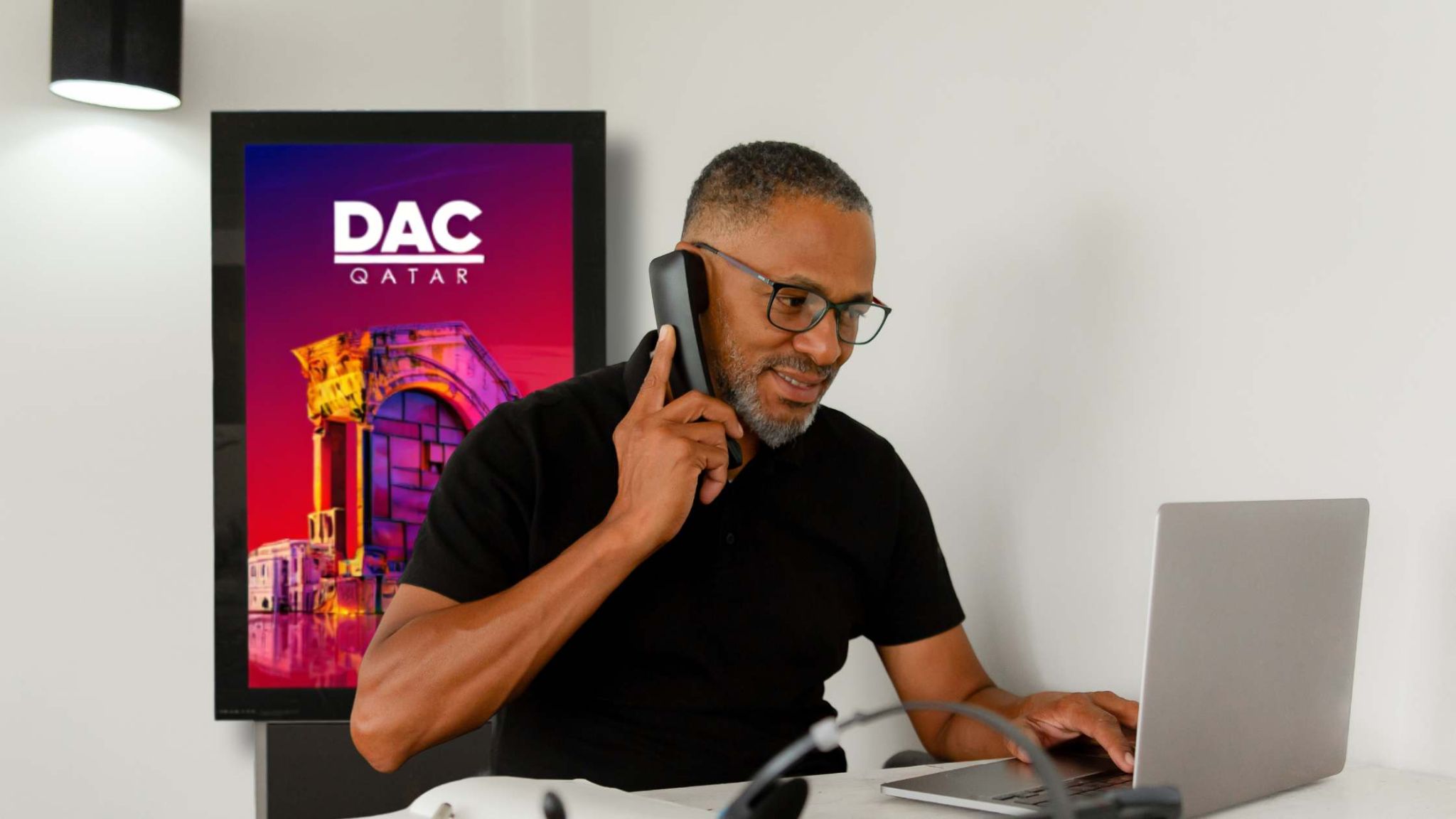 Professional customer support for digital signage solutions in Qatar – DAC Qatar Smiling customer support representative in Qatar providing service assistance via phone, with a DAC digital signage display in the background.