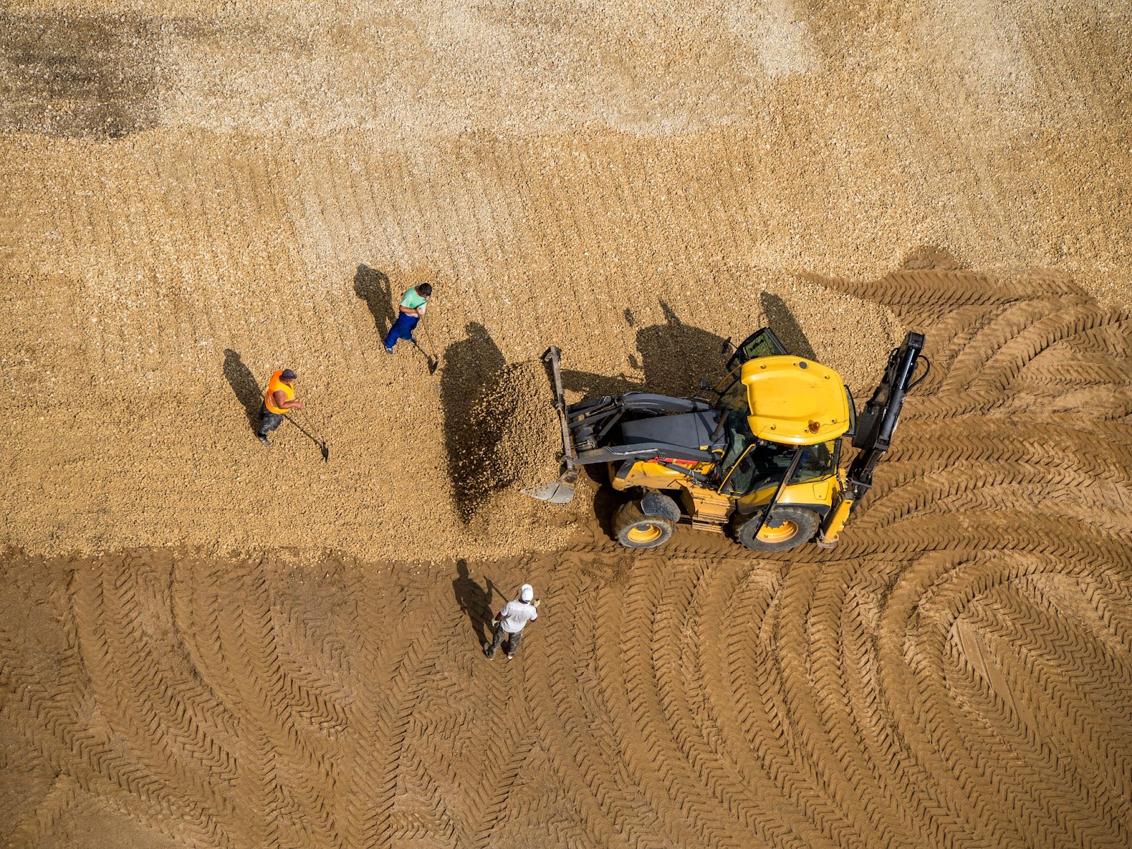 Aerial view of a wheeled loader grading land as workers shovel to shape terrain on a construction site.