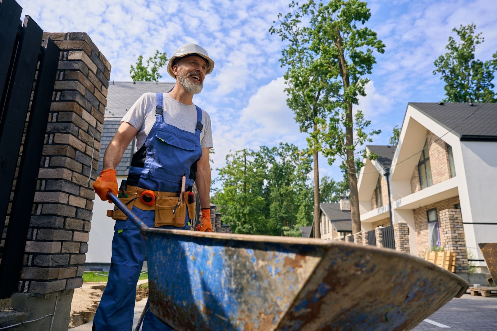 A residential concrete contractor using a wheelbarrow transfers building materials on-site, preparing for construction in a village.