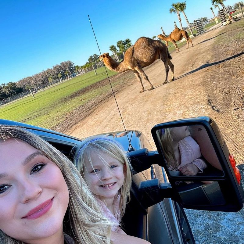 Mother and daughter smiling from safari vehicle with camels in background at Wild Florida Drive-thru Safari Park.