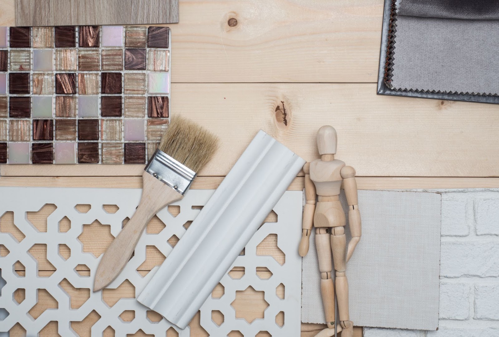 Various material samples for interior trims, showcasing decorative wall decors and tiles, a baseboard piece, a paintbrush, and a wooden doll for scale.