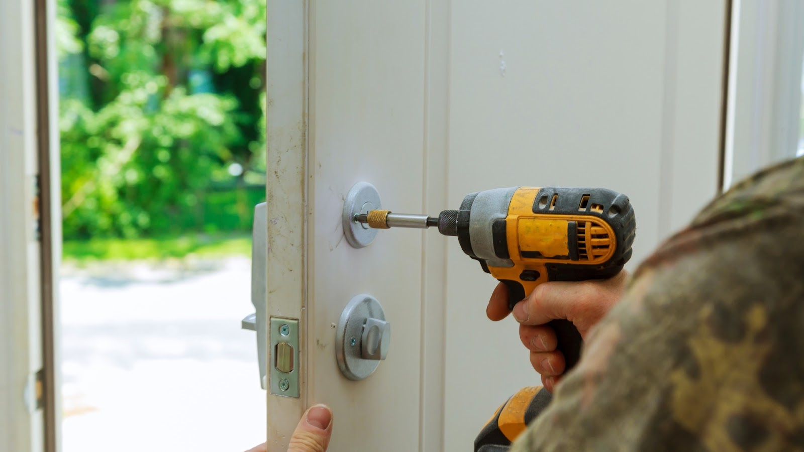 A locksmith uses a power drill to replace a lock on a door.