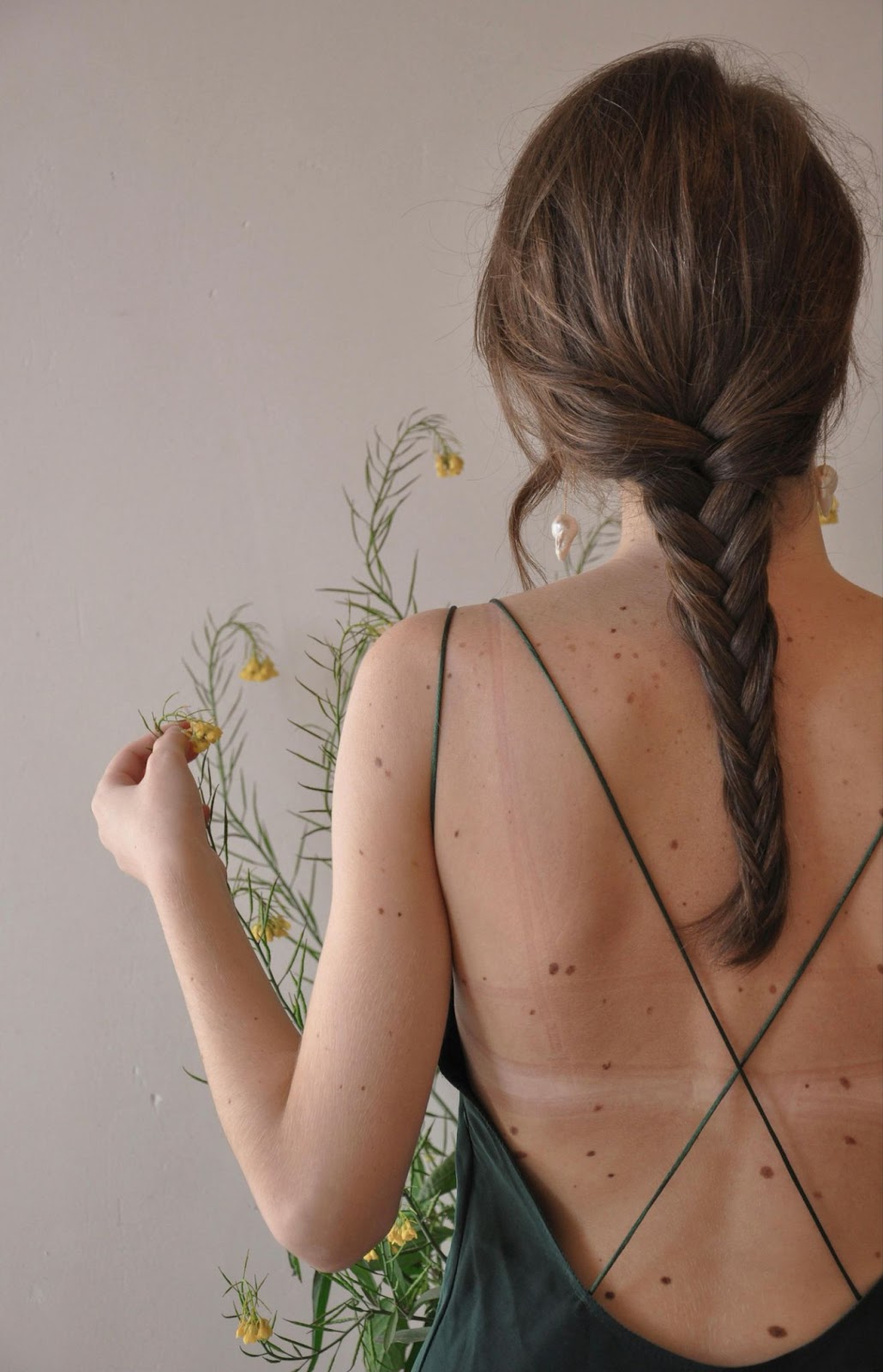 Brunette girl facing away from the camera showcasing her back in a low strap shirt with her clear skin due to using body oil