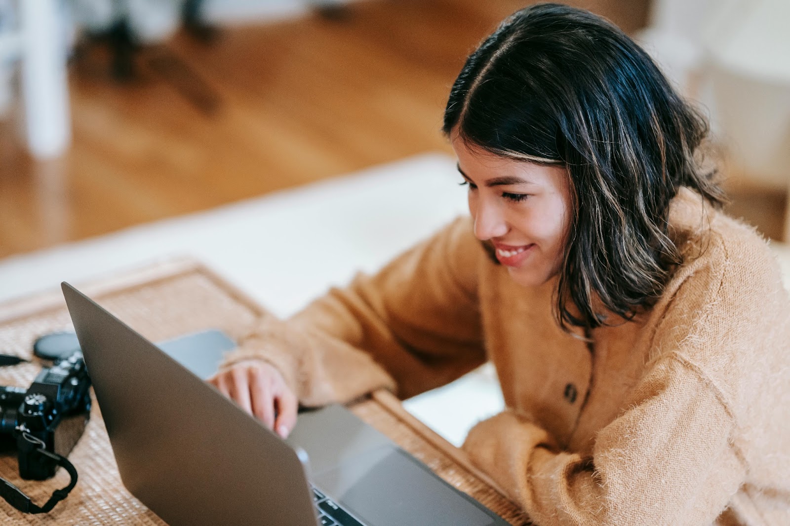 Young woman smiling while using a laptop at a wooden table 