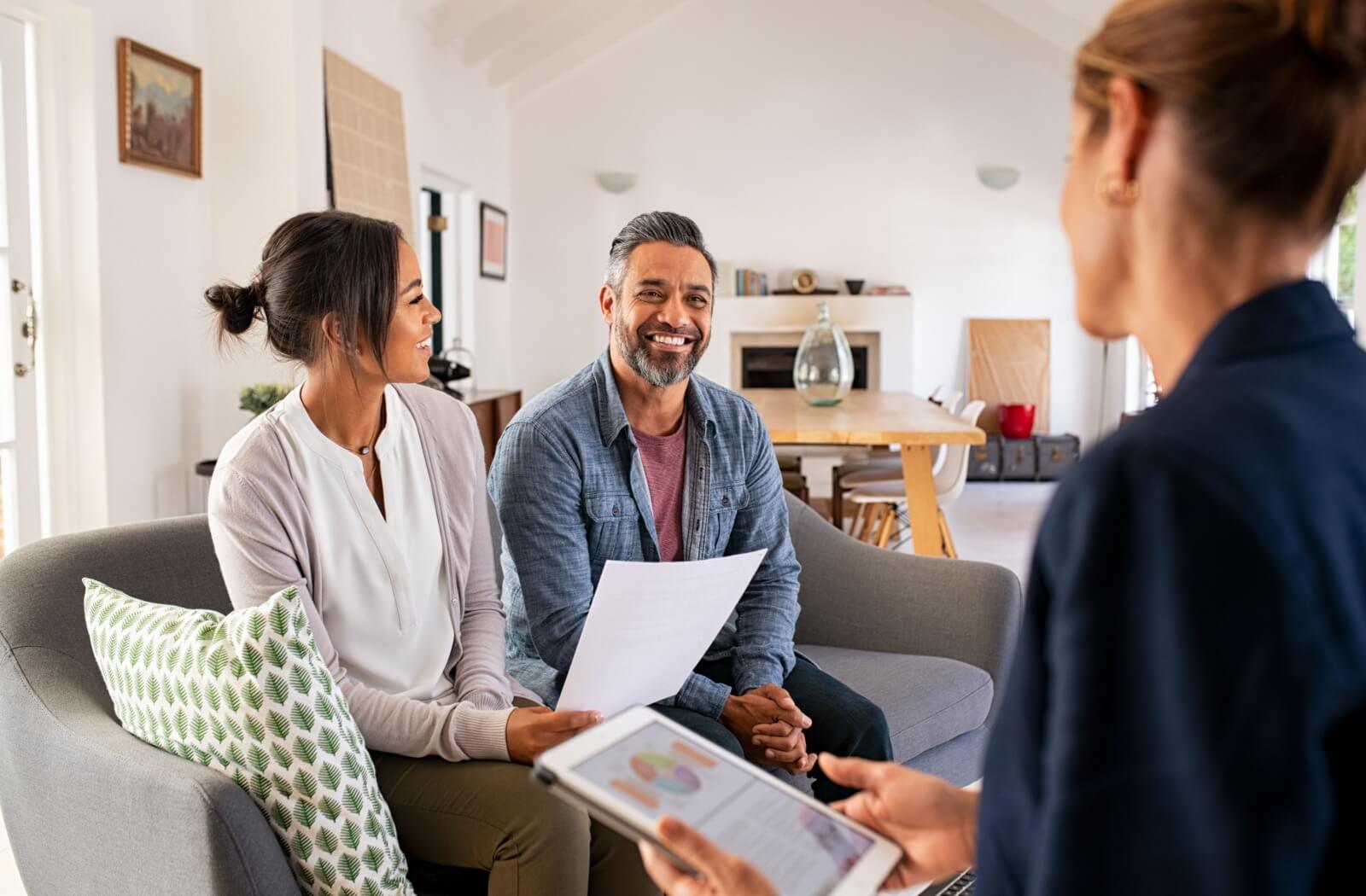 A couple sitting on a couch and smiling as they meet with a financial planner to discuss their lottery winnings.