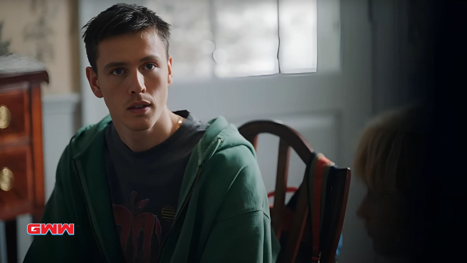 Harris Dickinsonn with short dark hair looking intently, standing in a room.