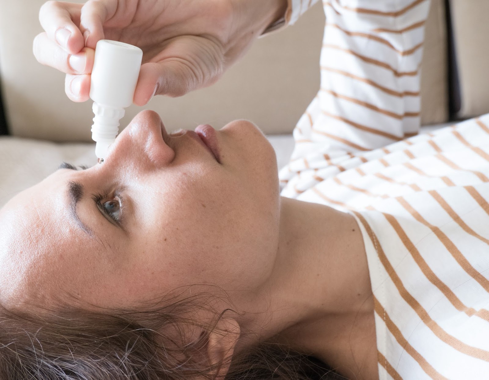 Woman applying artificial eye drops in bed to find relief for Blepharitis.