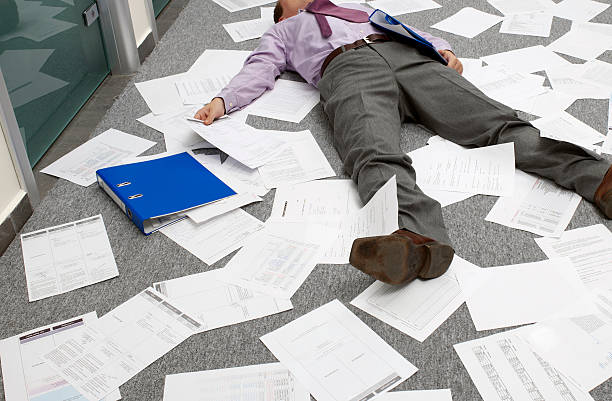 A person in office attire is lying on the floor, surrounded by scattered papers of their design portfolio.