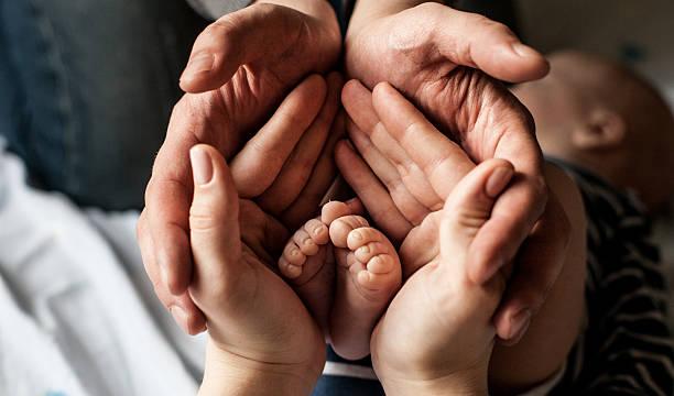 Little child foot in parents palms young family of mother of the father and kid. Mother and the father hold legs of the newborn child in the palms. birth mother father stock pictures, royalty-free photos & images