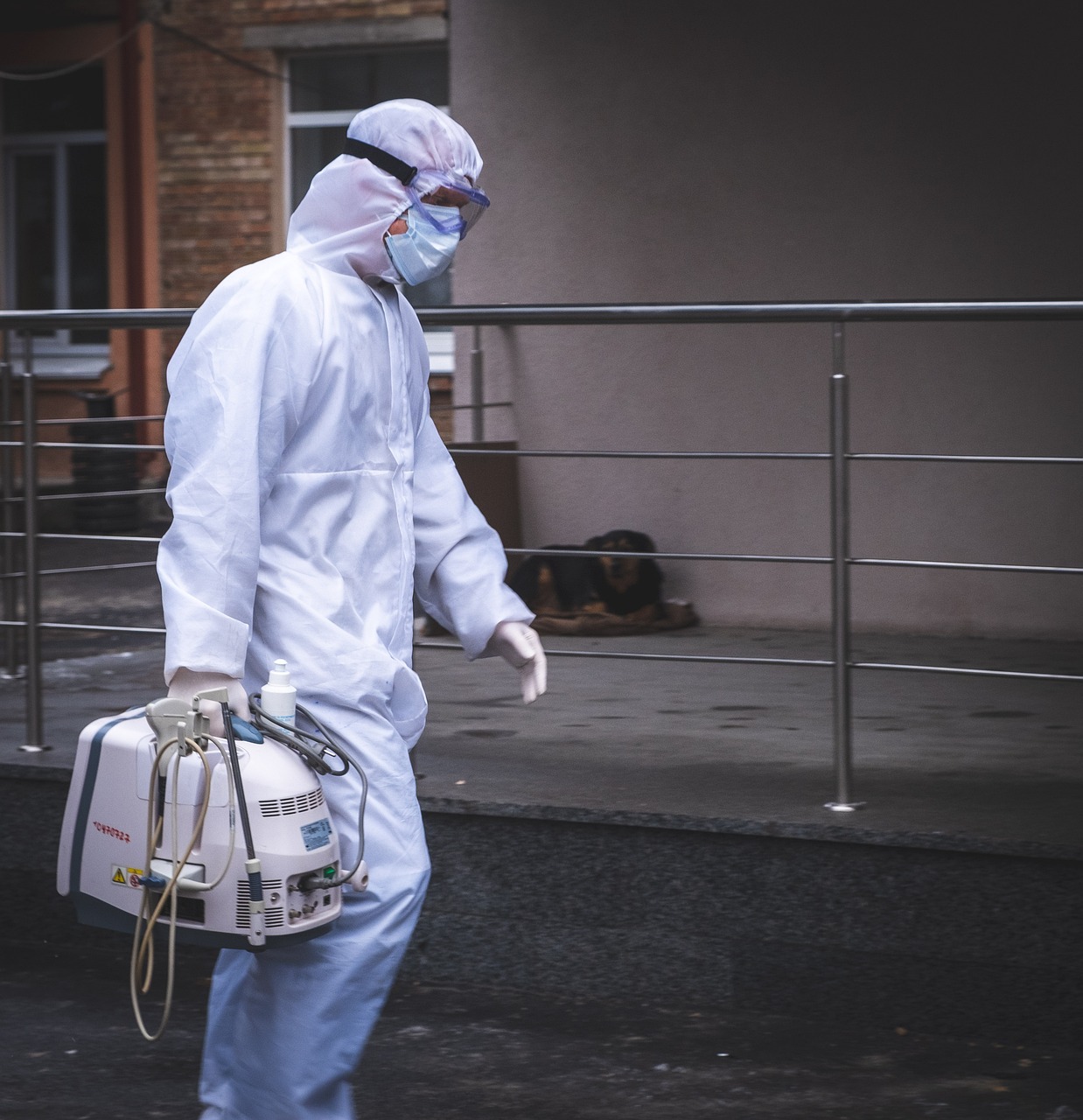 A person wearing a protective suit, goggles, and a face mask while carrying a foam insulation sprayer. 