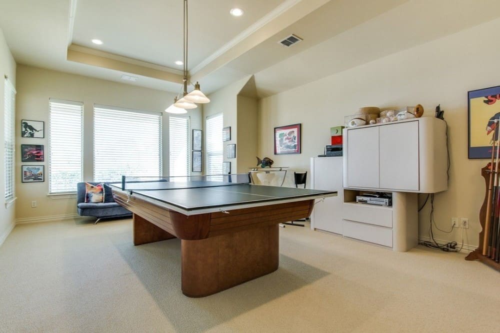 Recreation room with white cabinets, a blue sofa, and a ping-pong table topped with glass dome pendants.