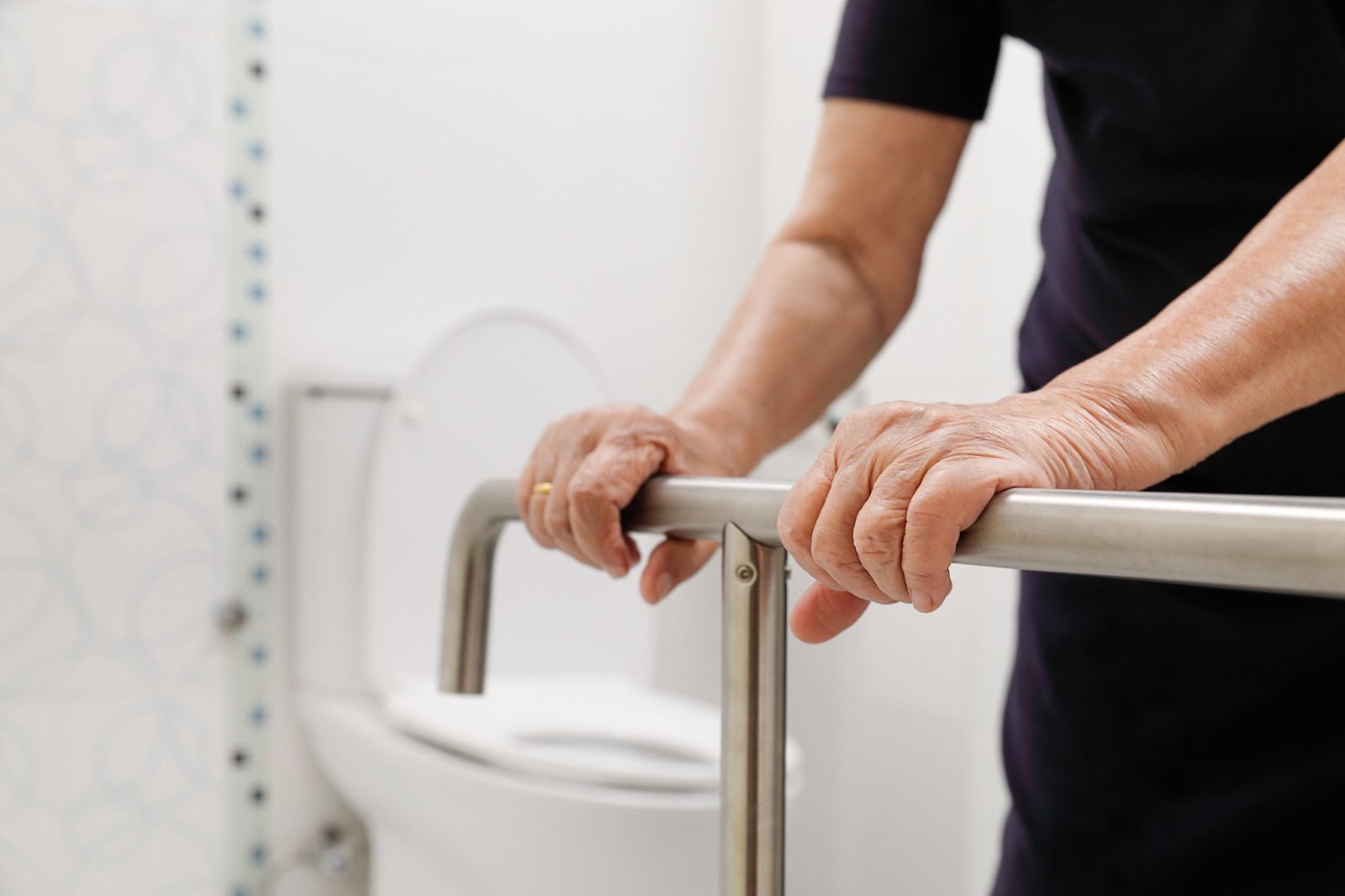 An older adult woman holding a handrail in a bathroom.