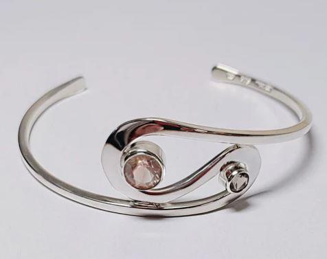 A silver bracelet with a stone in the middle

Description automatically generated