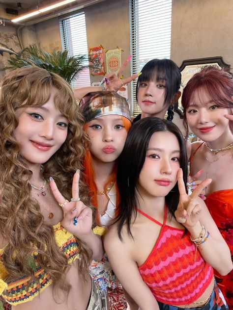 This contains an image of GIDLE group members posing for the camera with their fingers in the shape of two peace signs