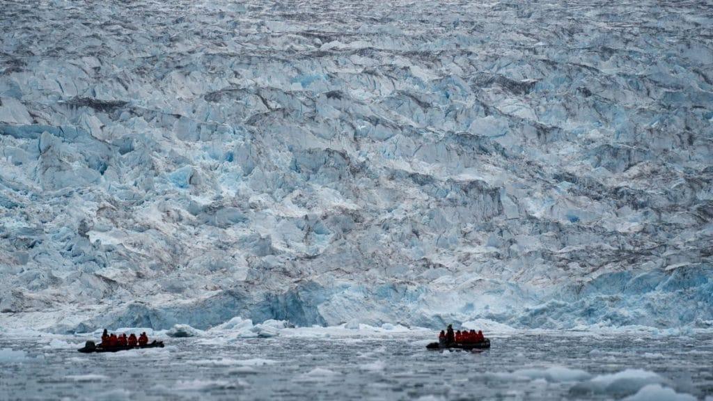 A boat in the water with a large glacierDescription automatically generated