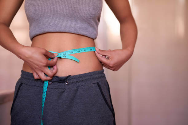 A woman measuring her waist with a tape measure, reflecting her progress in weight management after stopping HRT.