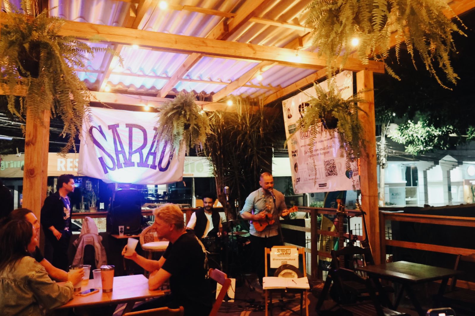 Visão geral do Lobitos Bar, com uma banda tocando ao palco e pessoas sentadas às mesmas. 