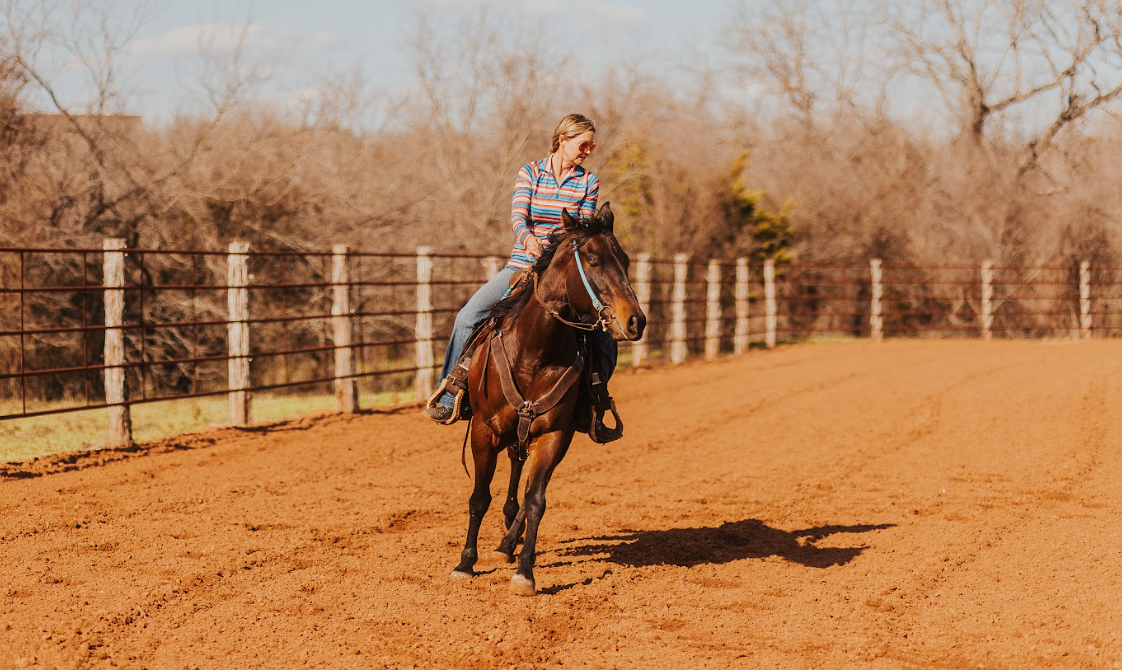 woman on horse back in middle of outdoor arena