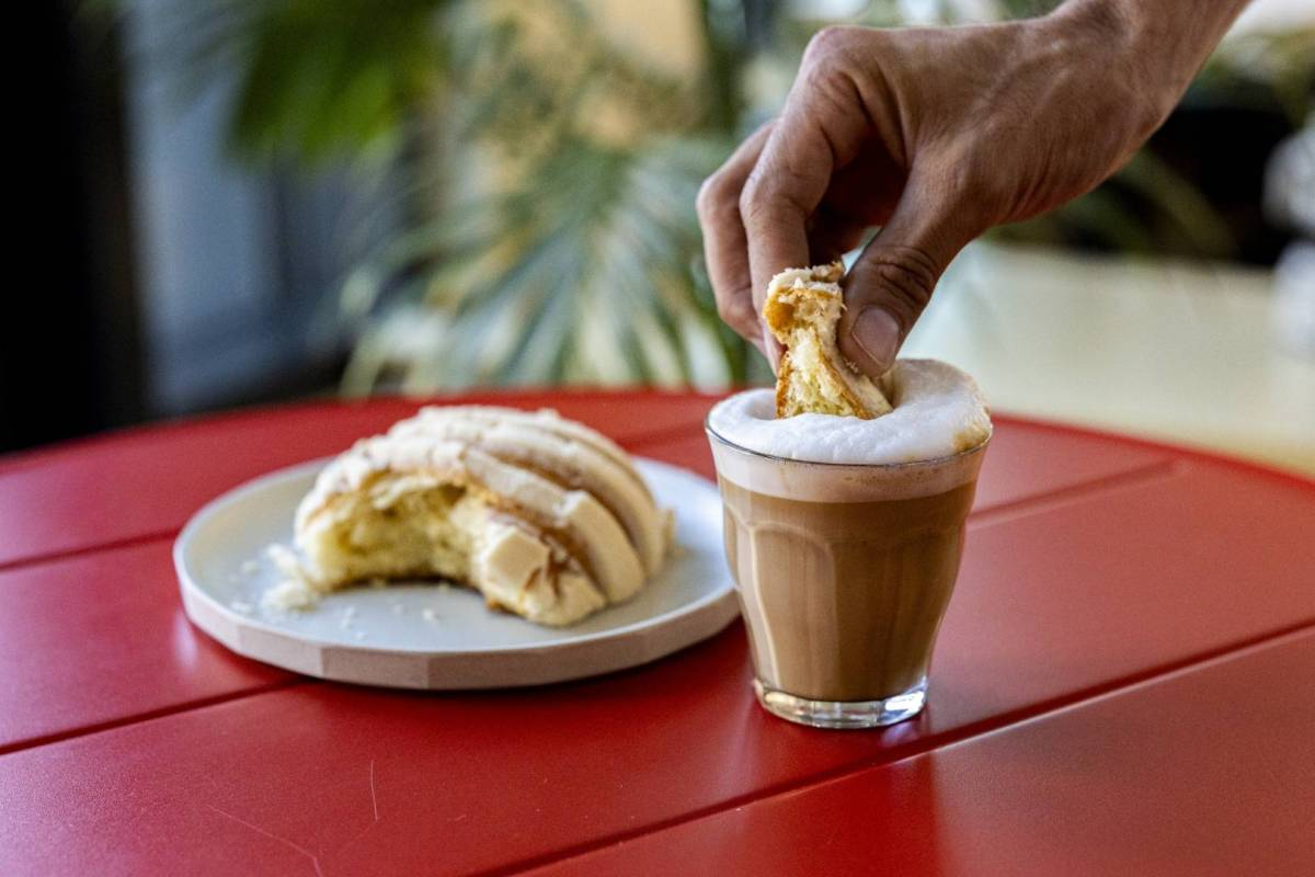 A hand dips a tasty looking pastry into a cup of coffee, on a red table