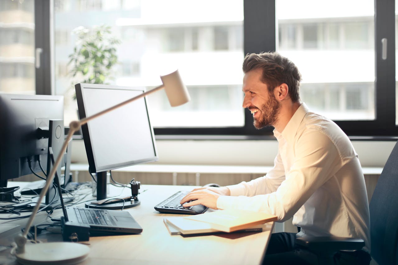 A man diligently working at his desk looking so happy while typing on his keyboard