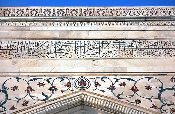 Close-up of a marble wall with intricate Arabic calligraphy and floral patterns, reminiscent of the architectural masterpiece that is the Taj Mahal in Agra.