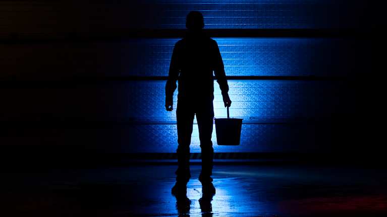 Photo shows a person standing with a bucket in their hand.