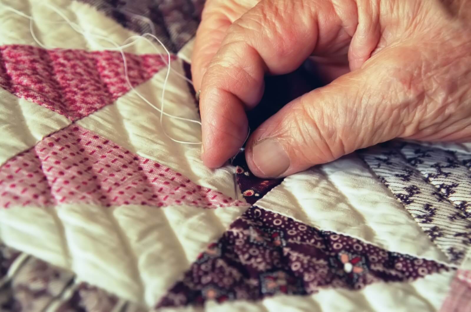 A close-up view of an older adult's hand quilting.
