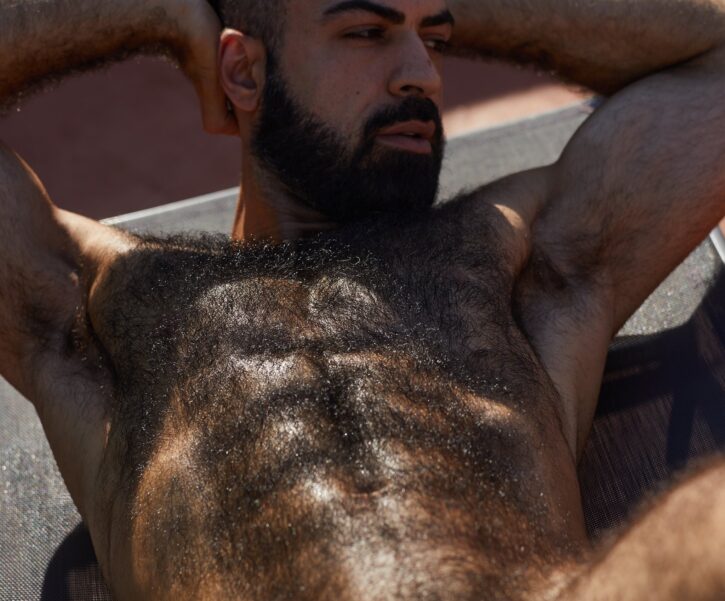 saleh helalat staring off into the distance with his arms behind his back showing off his extremely hairy abs and chest