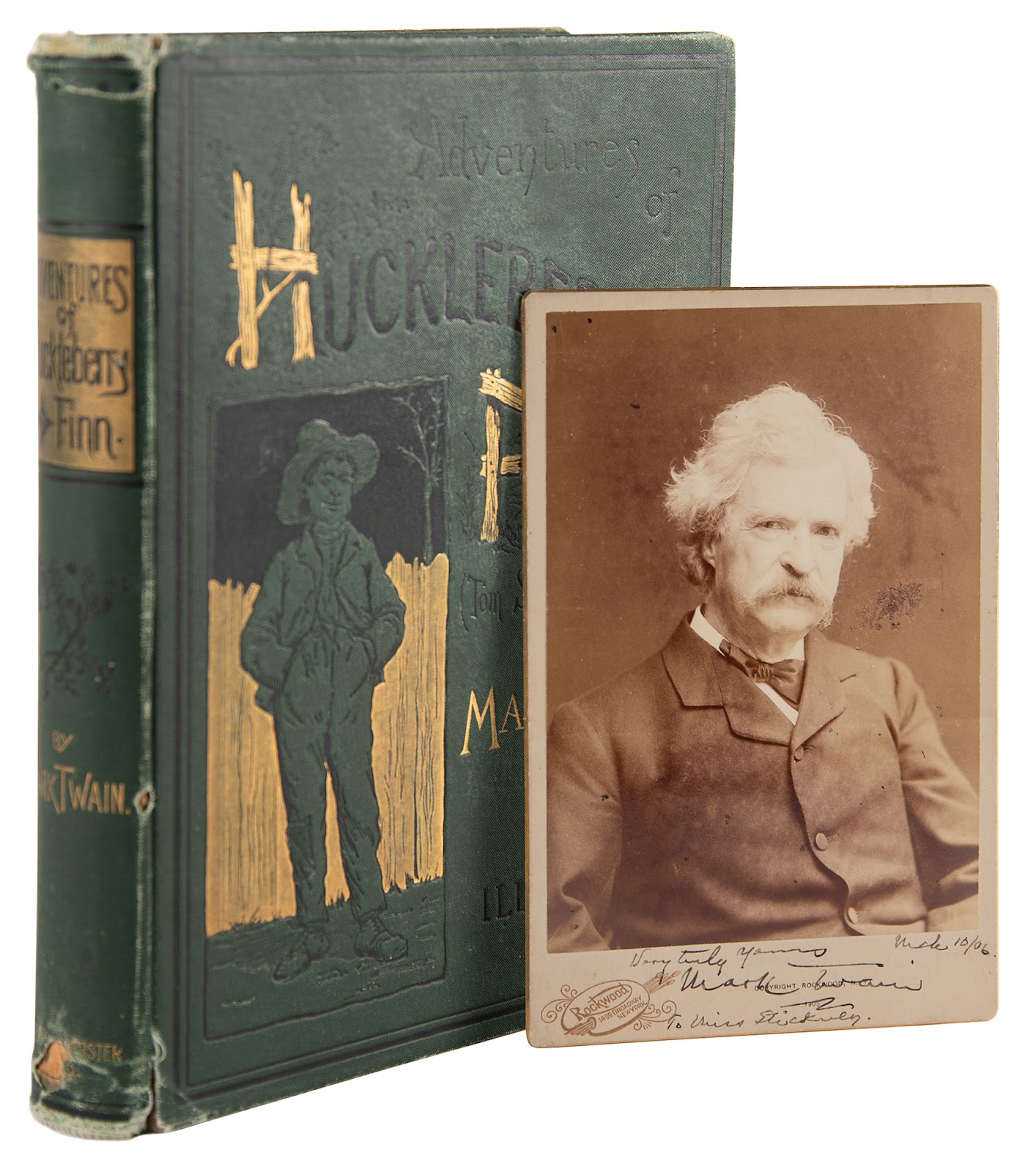 4.25 x 6.5 cabinet photo of Samuel L. Clemens by Rockwood of New York, nicely signed and inscribed on the mount in ink, "Very truly yours, Mark Twain, To Miss Stickney, March 10/06.” The photo is pictured with an American first edition of The Adventures of Huckleberry Finn.