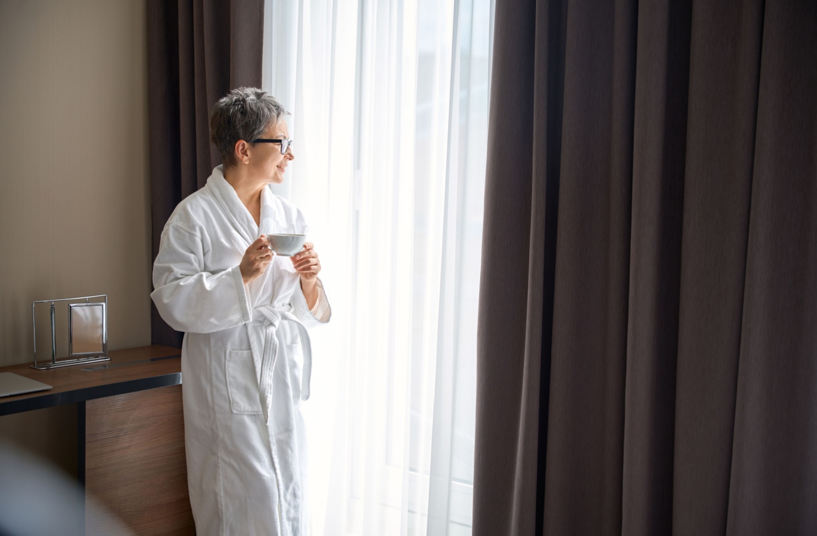 An older adult in a bathrobe enjoys a cup of coffee in their retirement living apartment.