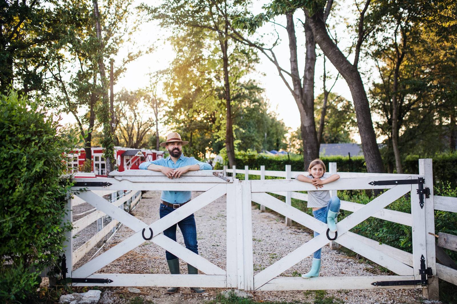 A father and daughter leaning on a wooden outdoor gate.