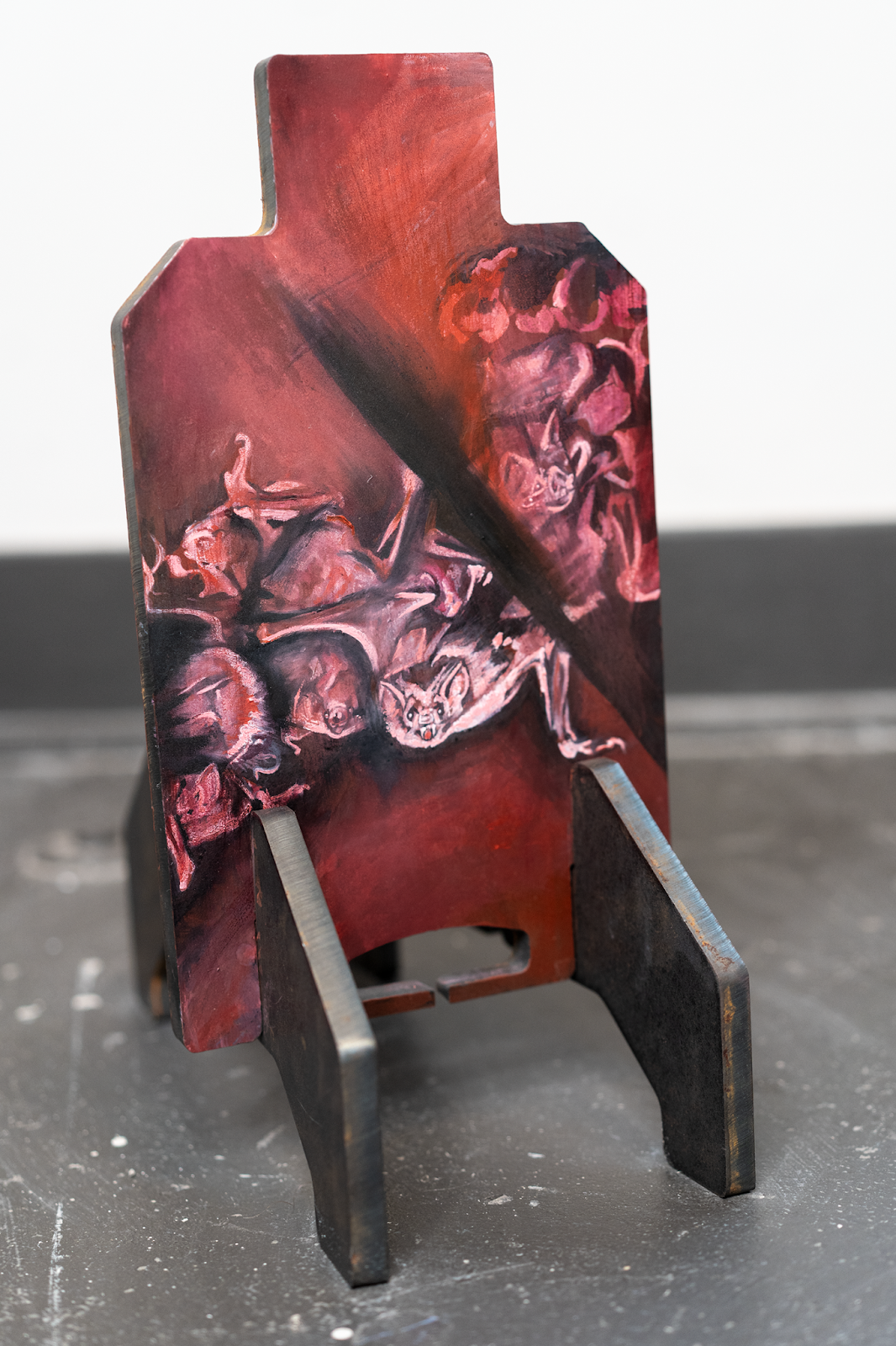 Image: D Rosen, Burning Alive, 2024, gouache and iron paint on steel shooting target, 13.5 x 7 x 0.375 in., 32.29 x 17.78 x 0.95 cm. An orange, red, pink, and black painting of Vampire Bats in a cluster burning. The painting is made on a steel shooting target which is freestanding and resting on a concrete floor with a white wall behind it. Photo: Levi Shand, Grant: DCASE, 2024.