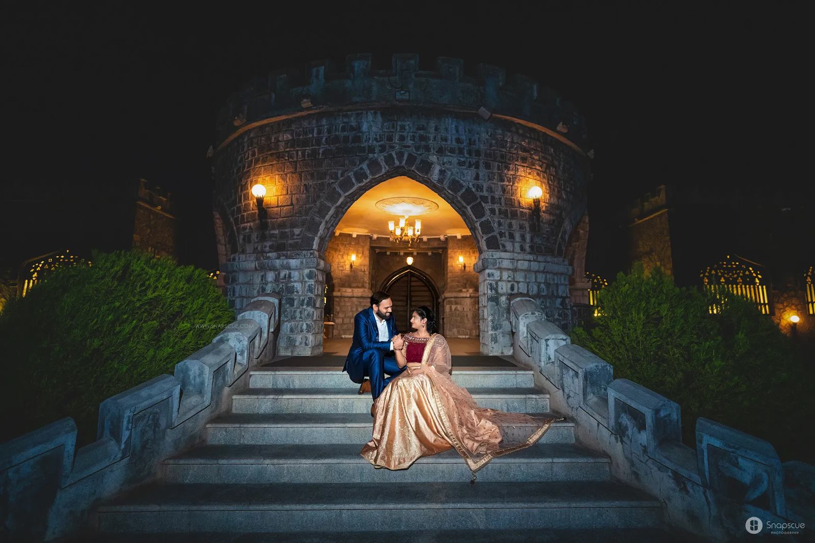 Charming pre-wedding photography of a couple sitting on stairs, with Shilparamam in the background