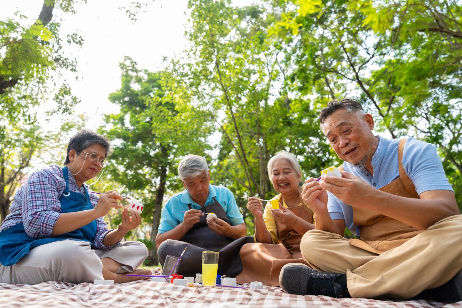 A group of older adults enjoys painting cactus pots outdoors in their memory care community.