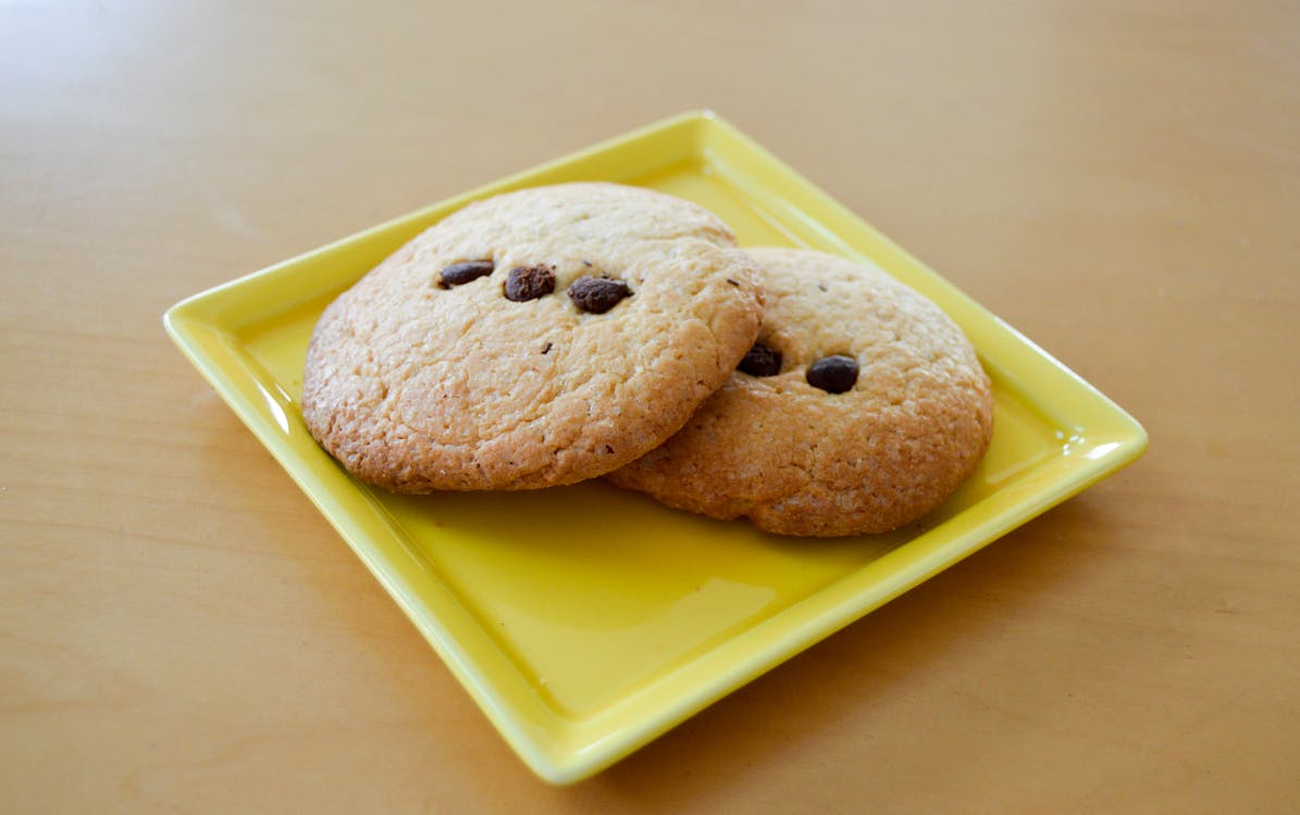 Free Two freshly baked chocolate chip cookies served on a yellow plate. 