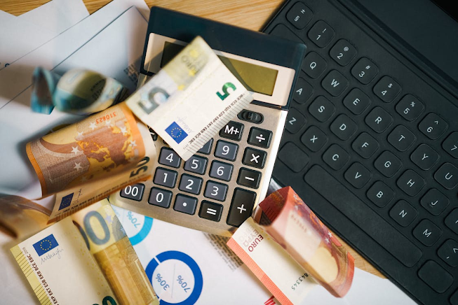 calculator with euro bills of five, ten, and fifty, black keyboard, and blue pie charts representing investment analysis and financial planning