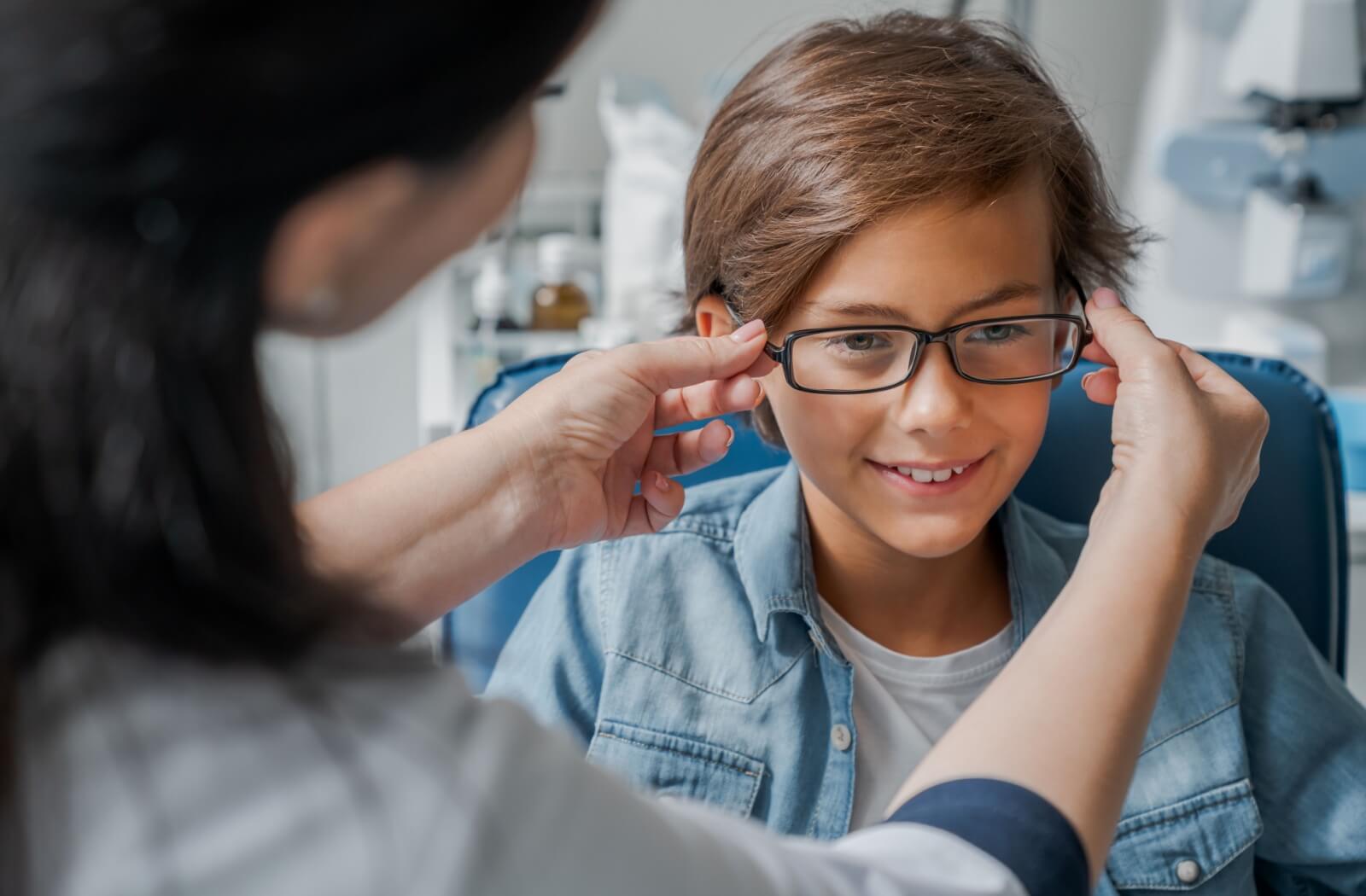 A young boy trying on his new glasses with myopia control lenses for the first time at his eye doctor's office.