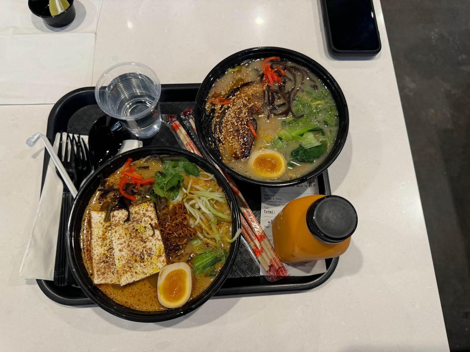 Two bowls of ramen on a black tray, placed on a white table. 