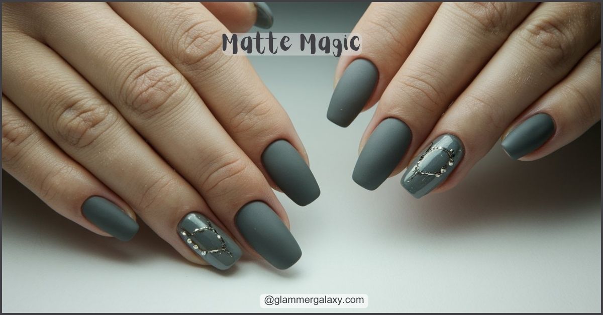 Matte gray manicured nails with silver gemstone accents on ring fingers, against a pale background.