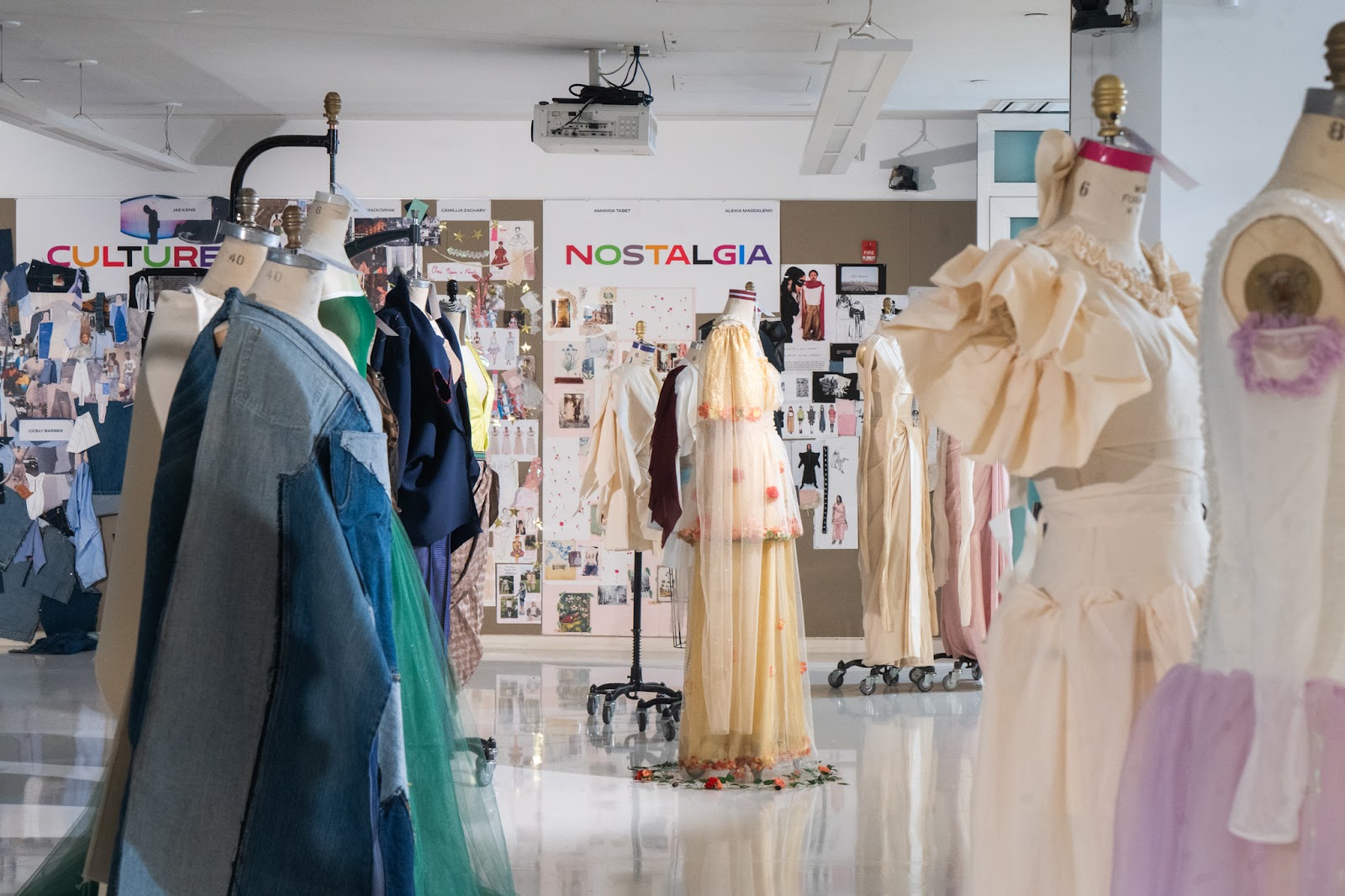 An exhibition space showcasing mannequins dressed in designs ranging from denim to elegant gowns with a backdrop of colorful moodboards. 