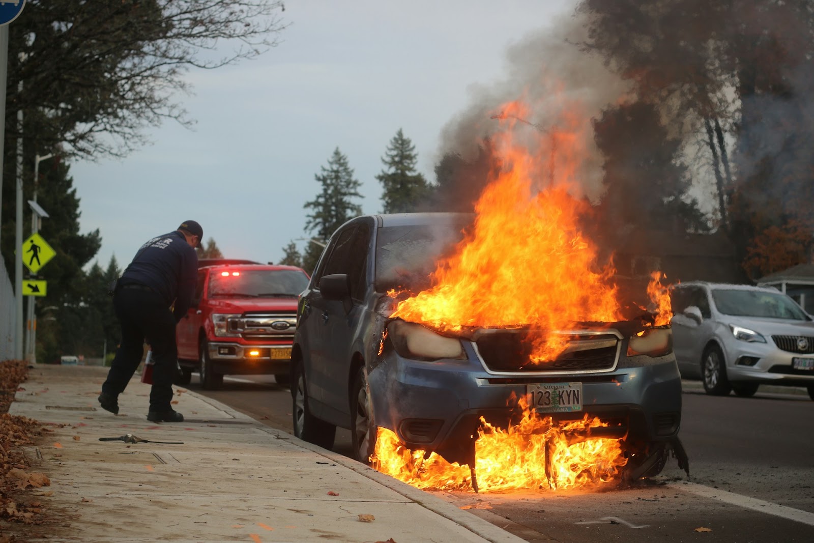 A man standing beside a burning car.