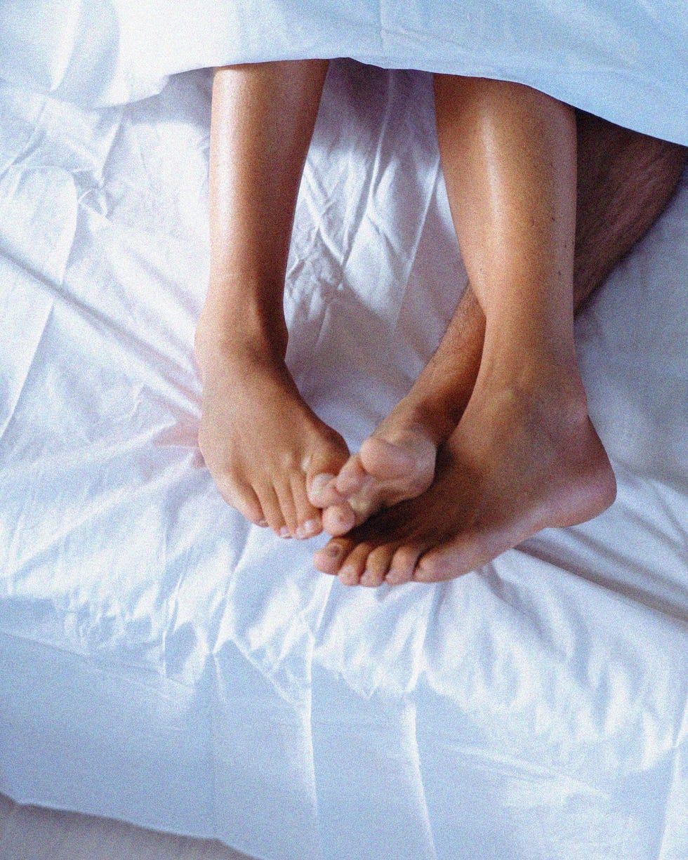 Intimate moment between two individuals in bed highlighting their feet