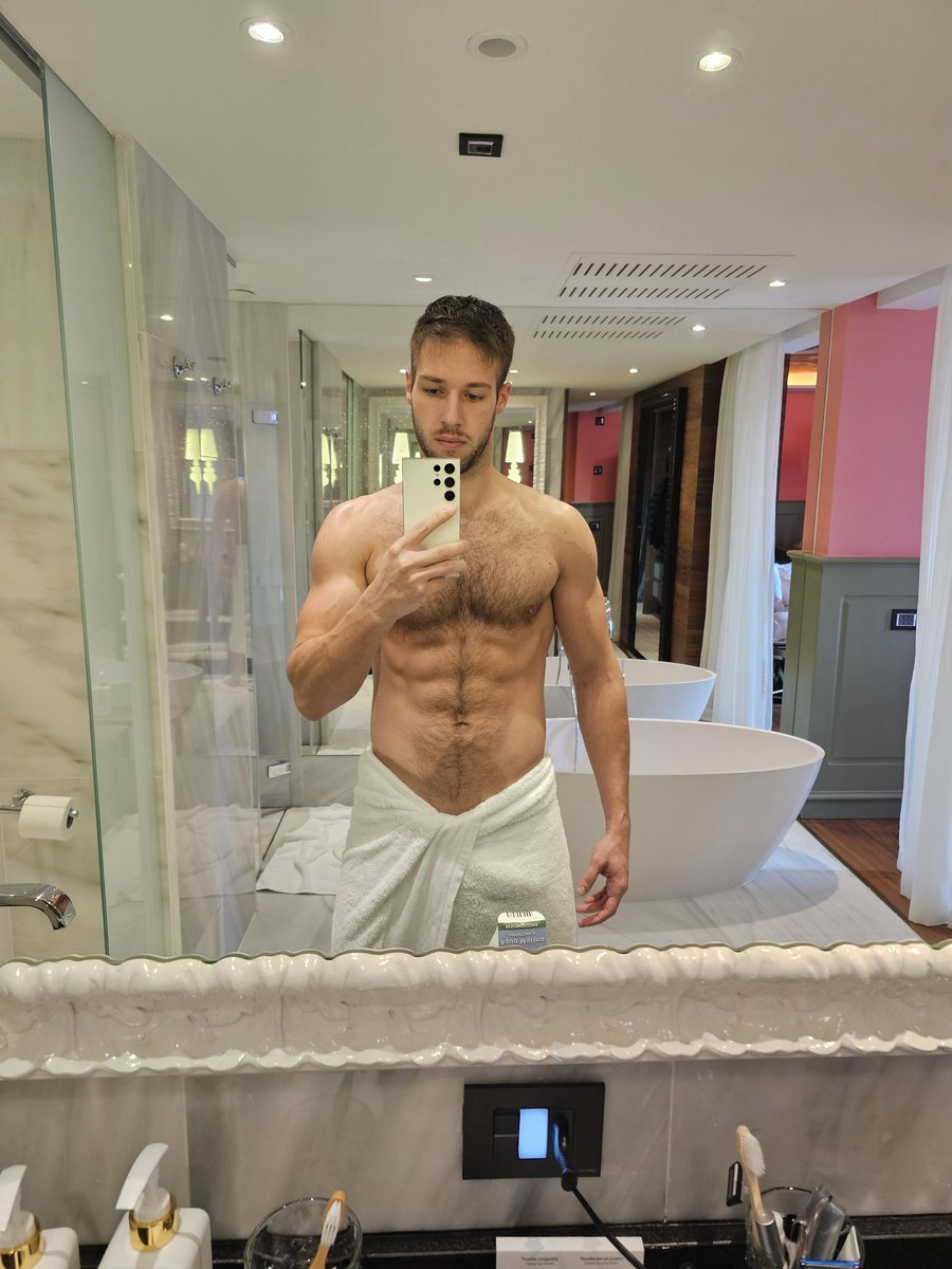 Arno Antino posing in a white towel showing off his erect cock through the fabric while taking an iphone mirror selfie in the bathroom for gay xxx onlyfans follower content