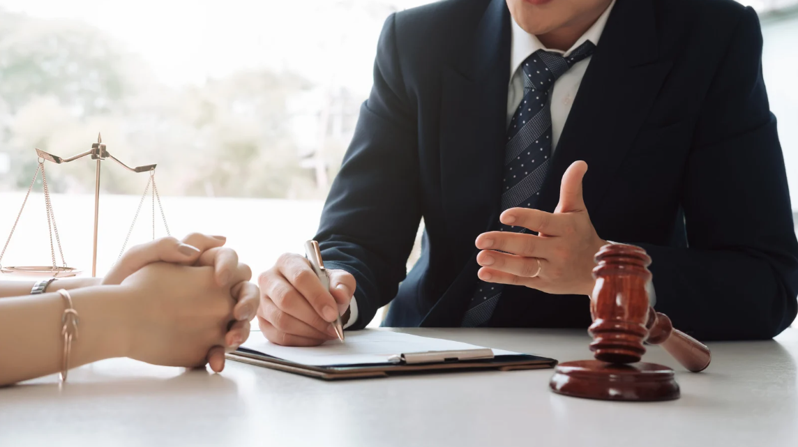 (Attorney consulting with a client at a desk, with legal scales and a gavel in view, symbolizing legal advice and protection of civil rights.)