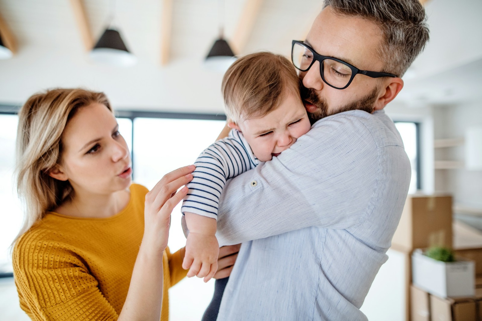 A mother and father with a crying baby. The father comforts the child, while the mother appears concerned, highlighting the stress of parental burnout.