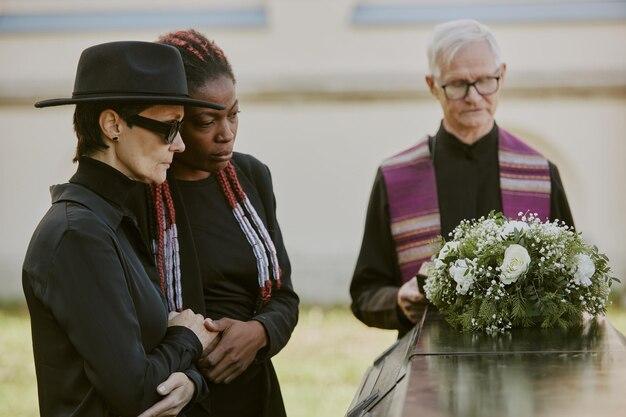 Grayhaired pastor reading prayer while mother and daughter bemoaning their loss