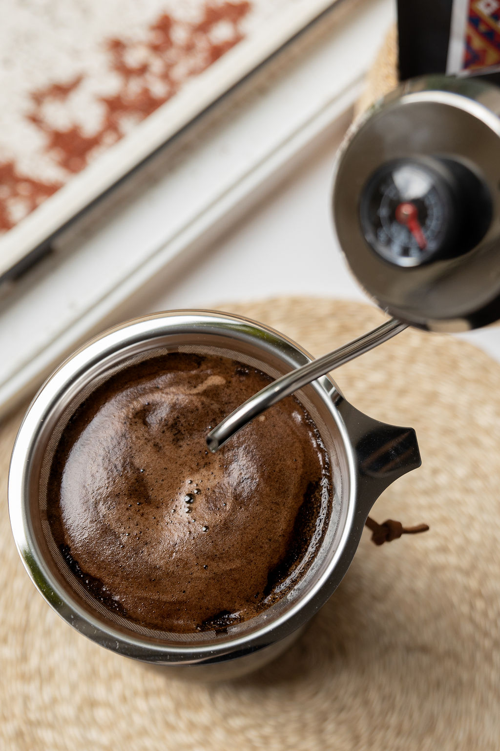 A close-up of freshly brewed Barako coffee in a French press, with its plunger resting on the coffee's surface. The press is on a beige textured mat near a window.