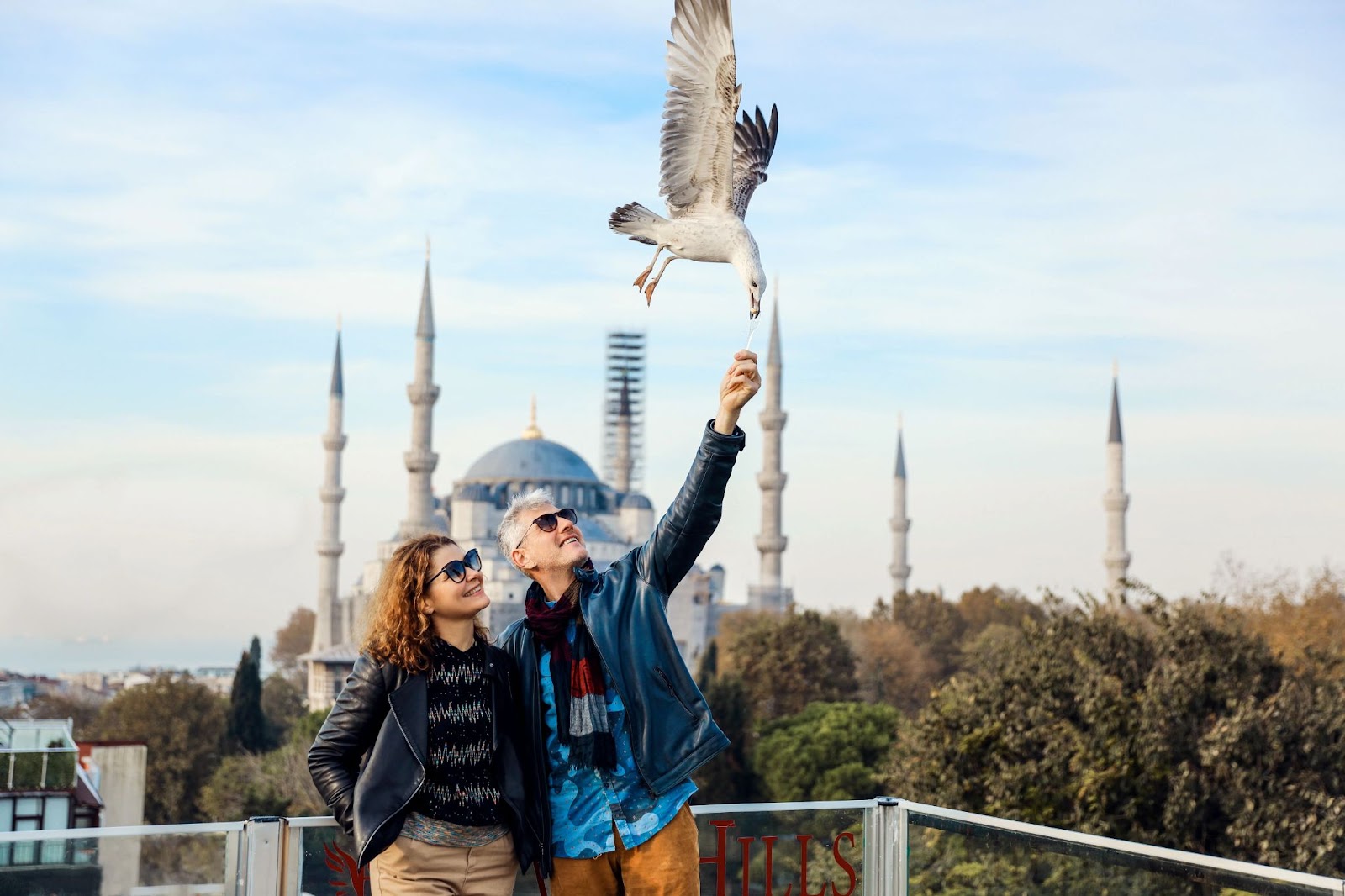 Couple feeds seagull on mosque-view balcony.